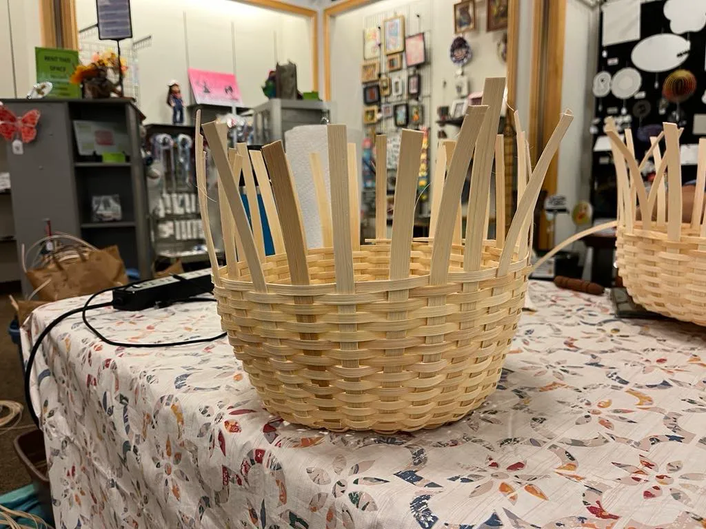 A round basket with upright spokes standing on a floral tablecloth inside the shop.