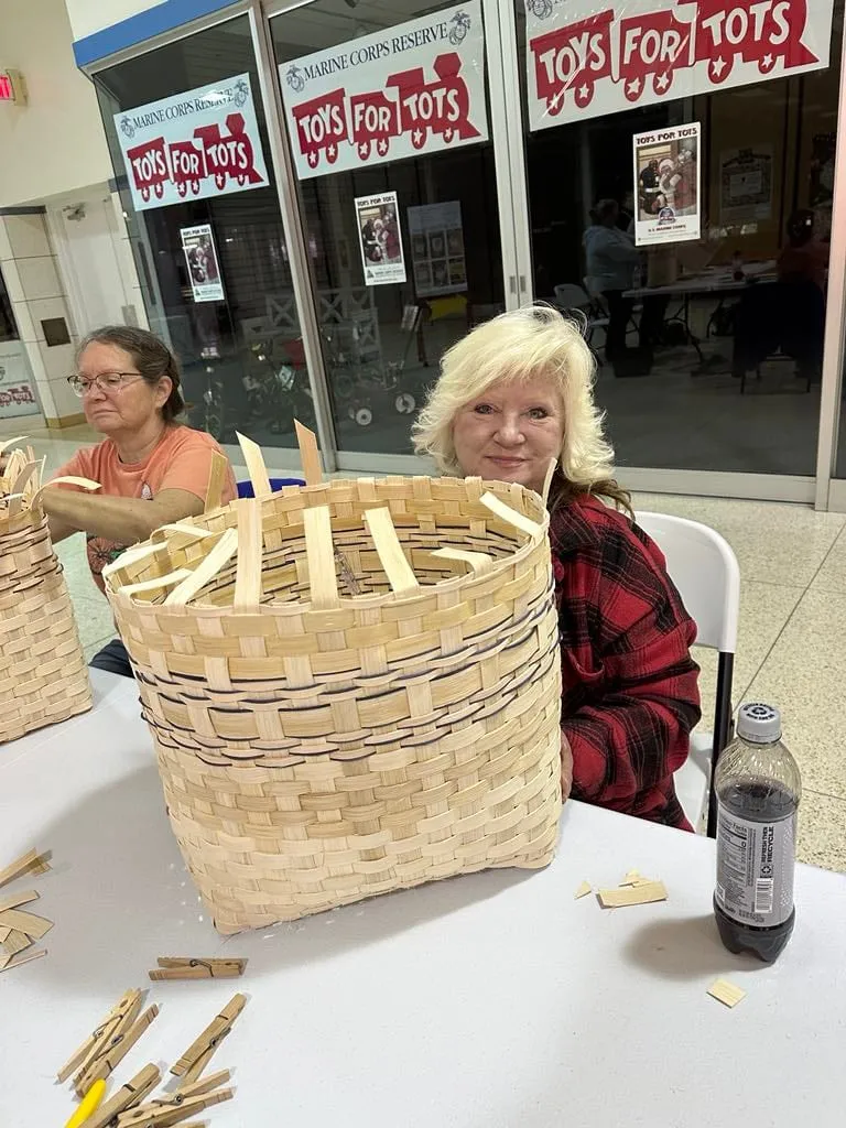 Two women at a table with a well-advanced basket, clothespins clamping the rim.
