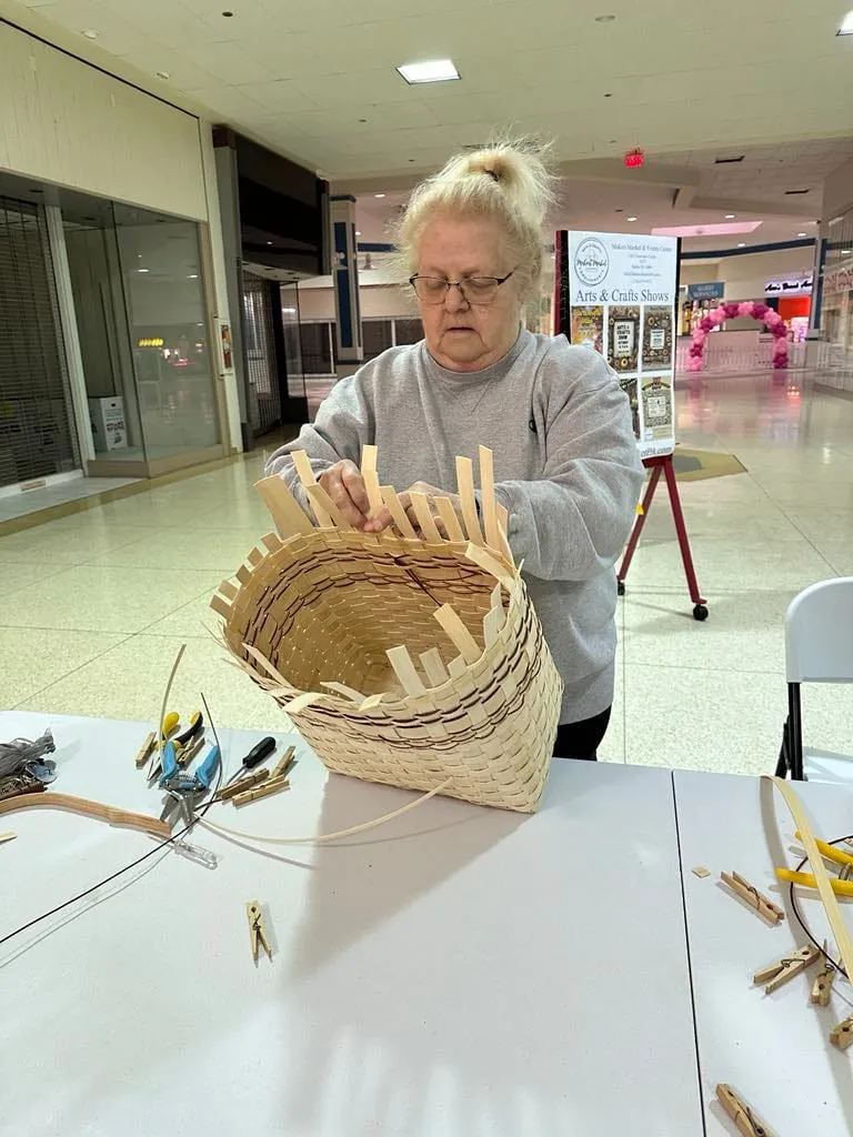 Woman handling a clothespin-clamped basket at a table in the mall corridor.