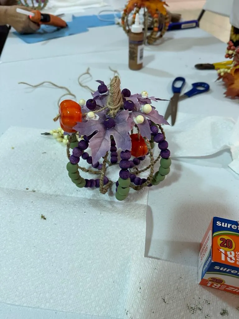 Close-up of a completed beaded pumpkin ornament in purple and green glass beads with a wire stem.