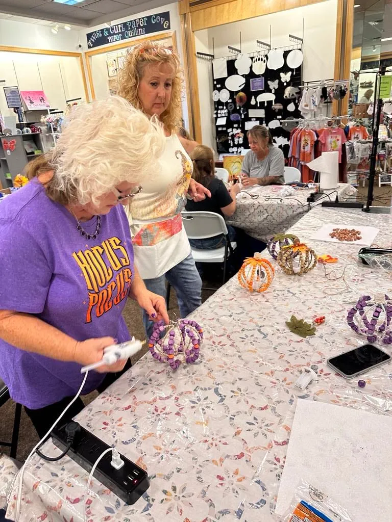 Two women at the class table with several finished beaded pumpkins in front of them.