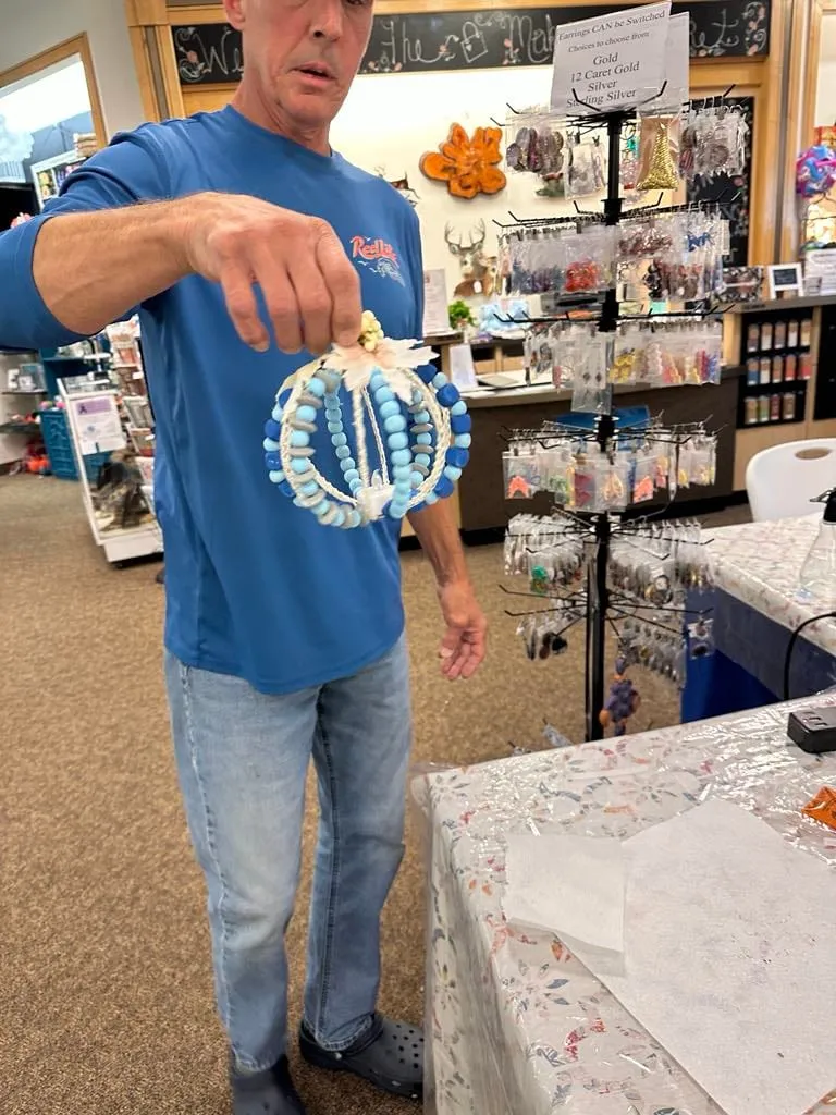Man in a blue t-shirt holding a completed white and blue beaded pumpkin toward the camera.