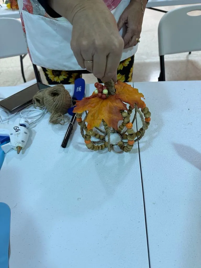 Close crop of hands attaching autumn leaves and berries to the top of a beaded pumpkin.