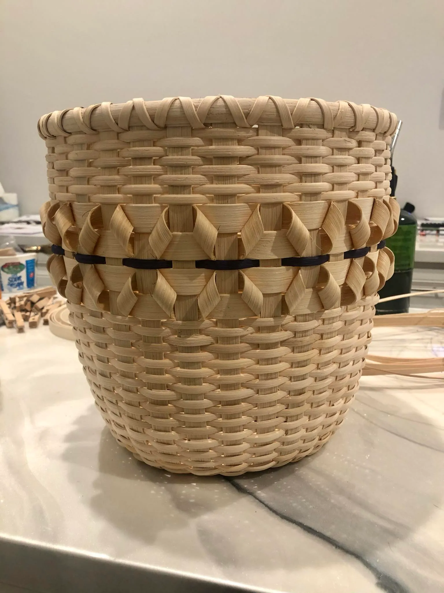 Finished tall cylindrical basket with a textured twill center band and dark accent stripe, on a marble counter.