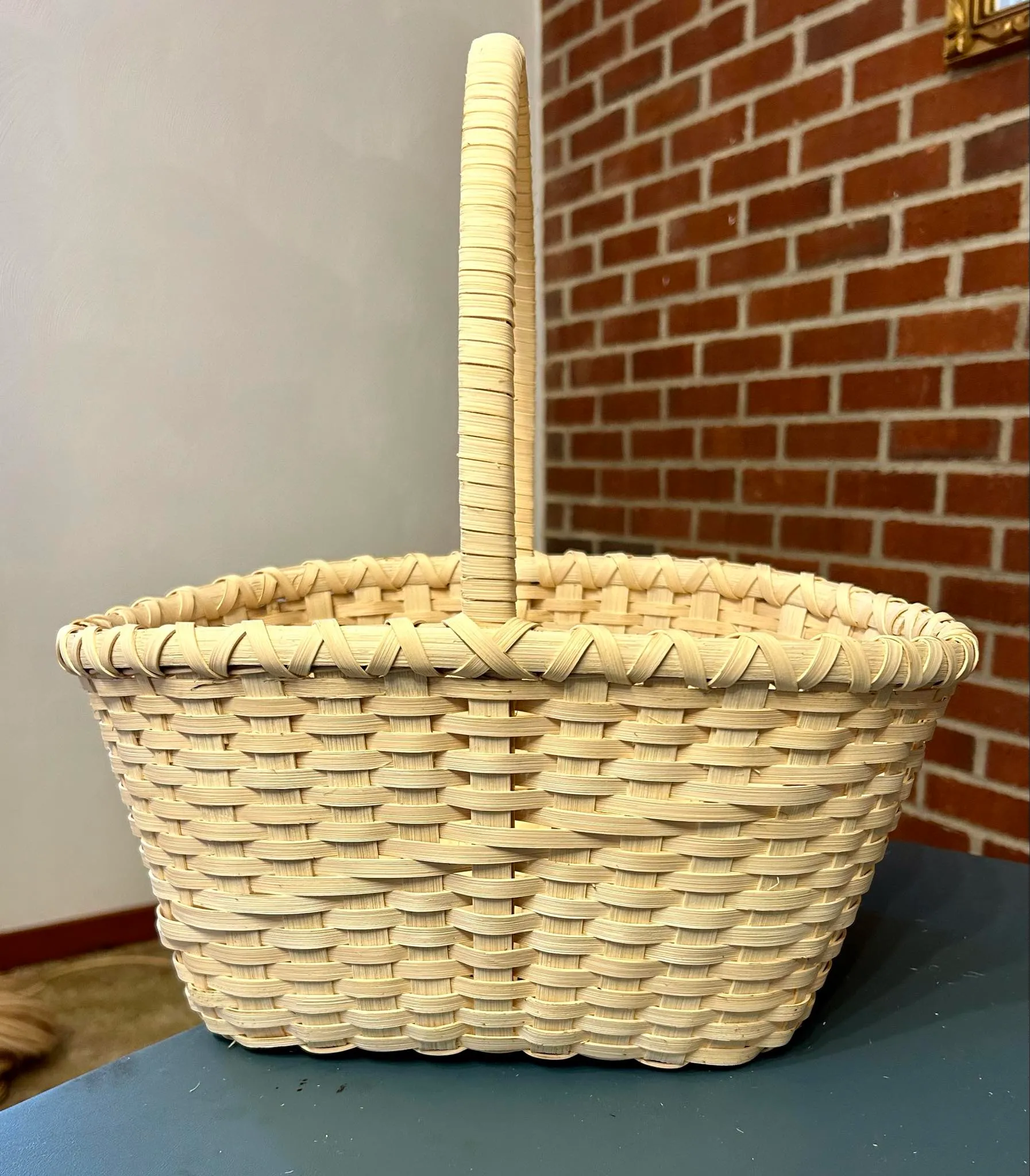 Finished rectangular market basket with a tall arched handle and plain woven body, on a slate surface.